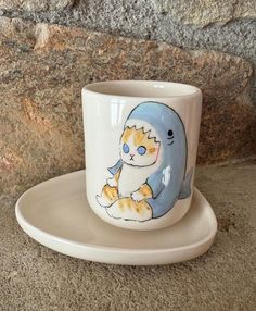 a coffee cup with a cat painted on it sitting next to a stone wall,