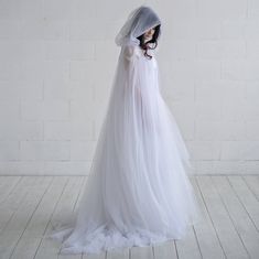 a woman in a white wedding dress with a hood on her head and veil over her face