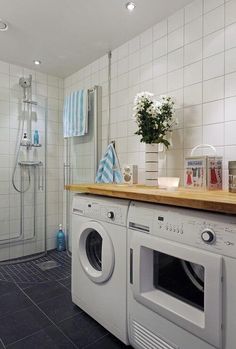 a washer and dryer in a bathroom with white tiles on the walls, along with a wooden counter top