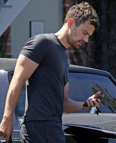 a man is looking at his cell phone while he stands in front of a car