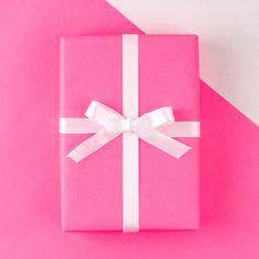 a pink gift box with a white ribbon and bow on the top, against a bright pink background