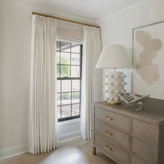 a room with a dresser, lamp and window