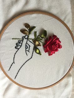 a red rose sitting on top of a white table cloth next to a embroidery hoop