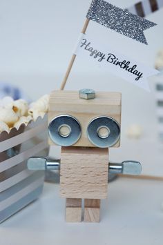 a wooden robot holding a happy birthday sign next to some cupcakes on a table