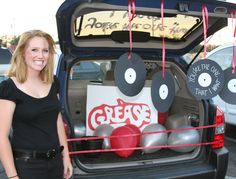 a woman standing next to the back of a car with its trunk open and decorations hanging from it