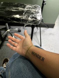 a person's arm with the word sonder tattooed on it, sitting in front of a chair