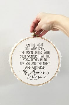 a hand holding up a cross stitch hoop with a quote on it that says, on the night you're born, the moon