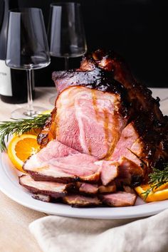 a plate with ham and oranges on it next to wine glasses in the background