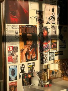 a wall covered in posters and magazines next to a white table with a lamp on it