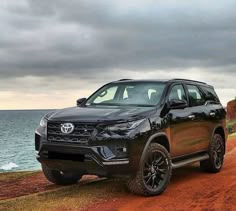 a black suv parked on top of a dirt road next to the ocean