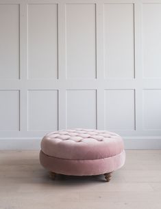 a pink ottoman sitting on top of a hard wood floor next to a white wall