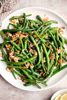 green beans with walnuts and garlic on a white plate next to a lemon wedge