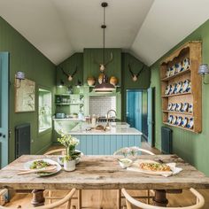 a kitchen with green walls and wooden table surrounded by chairs, plates on the counter