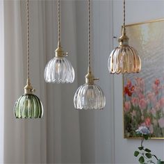 three glass pendant lights hanging from a ceiling in a room with white walls and flowers