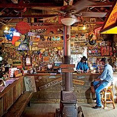 a man sitting in front of a wood stove inside of a store filled with lots of items