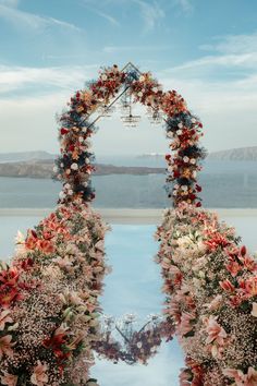 an arch made out of flowers on top of a white building with water in the background