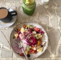 a bowl filled with fruit and yogurt next to a cup of coffee on a table