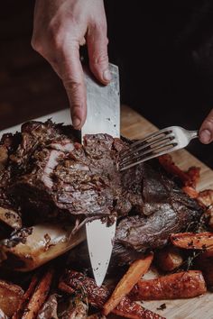 a person holding a knife and fork over a steak on a cutting board with potatoes