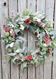 a wreath with red berries, green leaves and white flowers hanging on a wooden fence