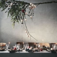 the table is set for christmas dinner with silverware and ornaments hanging from the branches