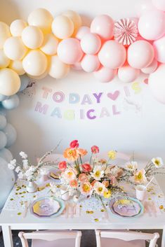 a table with flowers and plates on it in front of some balloons that say today is magical