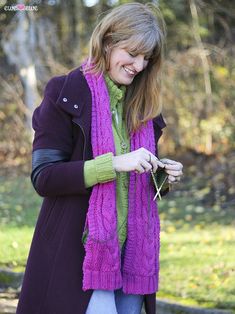 a woman in a purple coat and green scarf is looking at her cell phone outside