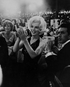 marilyn monroe clapping at an event with her hands in the air and two men standing behind her