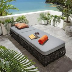 an outdoor daybed with orange pillows and sunglasses on the ground next to some plants