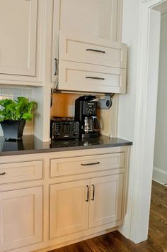 a kitchen with white cabinets and black counter tops is shown in this image, there are two coffee makers on the counter