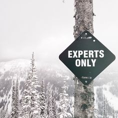 a black and white sign that says experts only on the side of a snow covered mountain