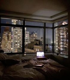 a laptop computer sitting on top of a bed in front of large windows at night