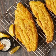 three fried fish fillets on a cooling rack with lemon wedges next to it