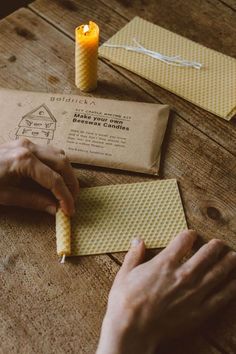 a person holding a lit candle on top of a table next to some envelopes