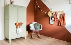 an orange and white room with clothes hanging on the wall next to a green cabinet