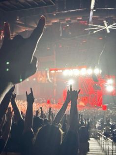 a crowd of people at a concert with their hands up in the air and lights on