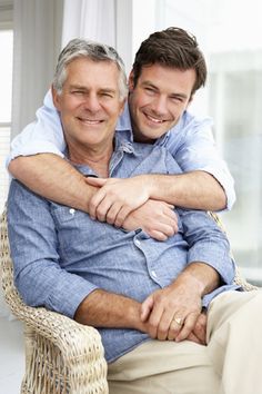 two men sitting on a wicker chair, one is hugging the other's chest