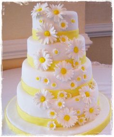 a white and yellow wedding cake with daisies on it