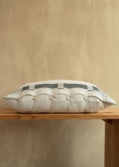 a white and black pillow sitting on top of a wooden table next to a wall