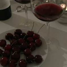 some cherries are on a plate next to a glass of wine