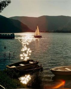 two small boats on the water with mountains in the backgroung and sun reflecting off the water