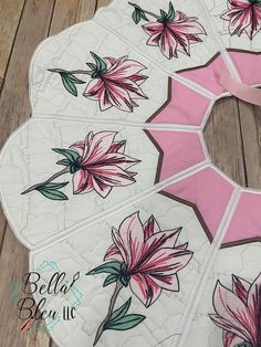 a pink and white quilted table runner with flowers painted on the side, sitting on a wooden floor