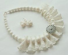 a white necklace and earring set on a white tablecloth with beads, pearls and lace