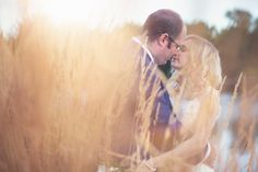 a bride and groom are standing in tall grass by the water with their arms around each other