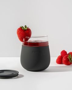 two strawberries sit on the table next to a wine glass with liquid in it