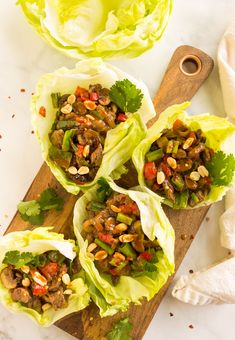 lettuce wraps filled with meat and vegetables on a cutting board next to a knife