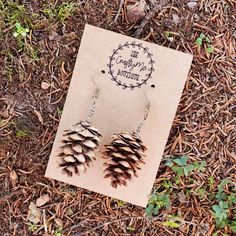 a pair of pine cone earrings sitting on top of a piece of paper in the grass