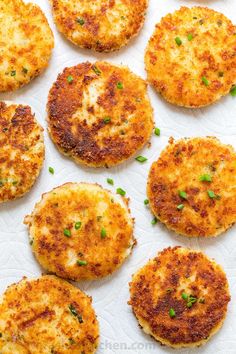 several crab cakes are arranged on a white paper towel with green onions sprinkled on top