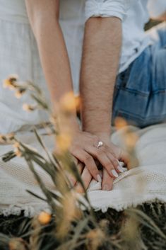 two people holding hands while sitting on the ground with flowers in front of their faces