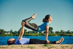 a man and woman are doing yoga on the sand by the water with their hands in the air