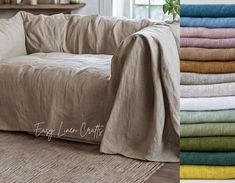 a couch covered in blankets and pillows next to a stack of folded linens on the floor